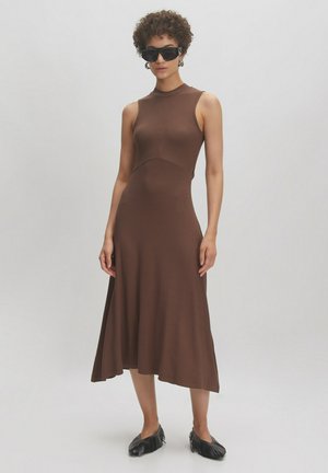 Braunes geripptes Midikleid mit einem taillierten Oberteil und ausgestelltem Saum. Das Kleid hat einen hohen Kragen und wird mit schwarzen spitzen Flats kombiniert.