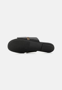 Crna klizna sandal s glatkom kožnom gornjom strukturom, širokim remenom, ravnim potplatom i suptilnim logotipom na dnu, koji prikazuje minimalistički stil.