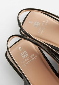 Schwarze Absatzsandalen mit strukturiertem Finish, featuring schmalen Riemen und einer gepolsterten beigen Innensohle. Branding sichtbar auf der Innensohle.