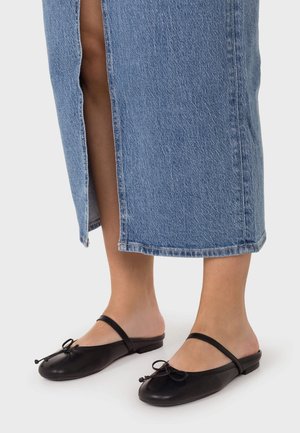 Piernas con una falda vaquera azul de longitud media y bailarinas negras de cuero sin talón, con una correa superior y un pequeño detalle de lazo.