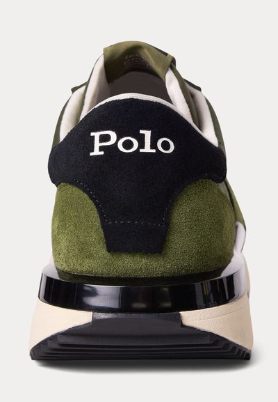 Žalios ir juodos zomšos sportinio batelio kulnas su baltu užrašu "Polo", balta tarpinė dalis ir juodos išorės pado detalės ant šviesaus fono.
