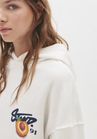 Felpa bianca con cappuccio caratterizzata da una grafica di pesca con la scritta "Sued. 91", realizzata in tessuto morbido con una vestibilità comoda.