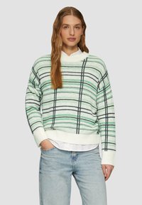 Gestreifter Pullover in Weiß mit grünen und schwarzen Streifen. Hat einen hohen Kragen, abgesenkte Schultern und gerippte Bündchen. Wird über einem weißen Hemd getragen.