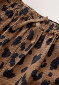 Brown fabric shorts with a textured finish, featuring a black spotted pattern and an elastic waistband with a drawstring for adjustment.