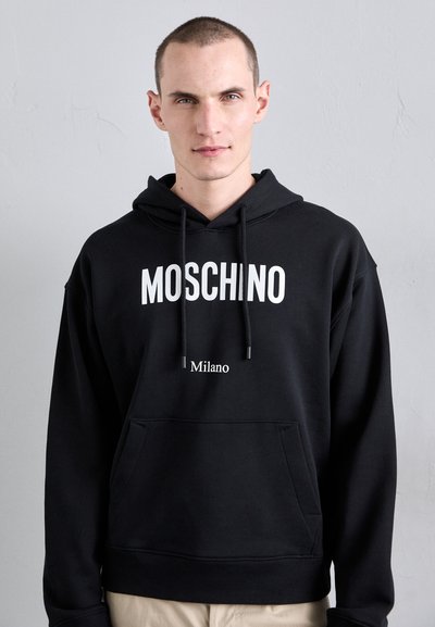 Hanorac negru dintr-un material moale, având un logo alb "MOSCHINO" și textul "Milano". Include un buzunar frontal și șireturi ajustabile.