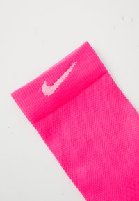 Helles rosa Nike Sportsock mit weißem Swoosh-Logo am gerippten Bündchen, flach auf weißem Hintergrund ausgelegt.