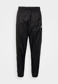 Černé lehké nylonové běžecké kalhoty Nike s elastickým pasem a manžetami, vybavené bočními kapsami na zip a bílým logem na stehně.