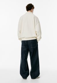 Hanorac crem supradimensionat cu guler, asociat cu blugi largi de culoare albastru închis, ce au două buzunare la spate. Design simplu și casual.