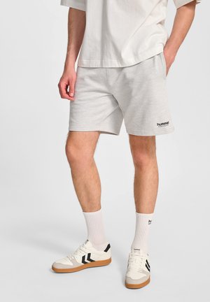 Hellgraue Baumwollshorts mit einem schwarzen "hummel"-Logo. Kombiniert mit weißen Sportsocken und weißen Sneakers mit schwarzen Streifen und Gummisohlen.