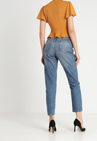 Hořčicový peplum top s krátkými volánkovými rukávy, doplněný o vysoké modré džíny a černé stileto podpatky.