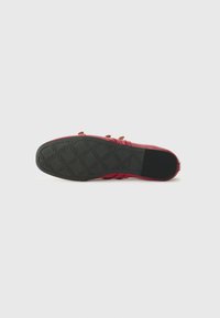 Scarpa rossa con tomaia in pelle liscia, caratterizzata da dettagli a strappo multipli. La suola è in gomma nera con un motivo di grip testurizzato.