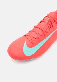 Crampons de football corail vif avec une tige texturée, affichant un grand swoosh aqua de Nike et des accents assortis, design lacé et crampons moulés.