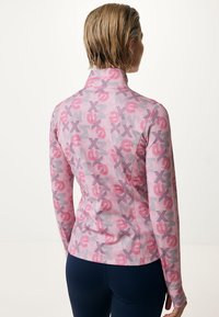 Maglia attillata a maniche lunghe di colore rosa con un motivo grafico ripetuto di lettere. Presenta un collo alto e un tessuto testurizzato, progettata per l'abbigliamento sportivo.