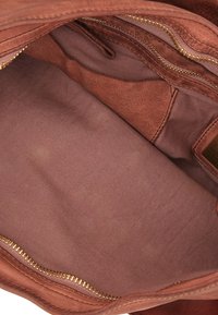 Interno della borsa a spalla in suede marrone con una foderatura in tessuto rosa liscio e uniforme. Presenta una chiusura a zip e una piccola tasca a scomparsa.