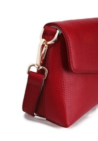 Červená kožená kabelka s texturovaným povrchem, ostrými tvary a zlatým kovovým zapínáním. Obsahuje odnímatelný popruh pro všestranné použití.