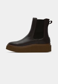 Zwarte leren Chelsea boot met elastische zijpanelen, voorzien van een dikke bruine ribbelzool en een trekflap aan de achterkant voor gemakkelijke instap.