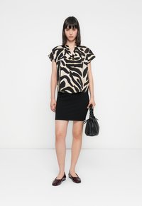 Svart og beige zebra-mønstret kortermet topp kombinert med et svart kroppsnært skjørt. Tilbehør inkluderer en teksturert svart veske og burgunder ballerinas.