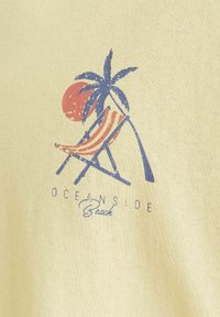 Lichtgeel stof toont een afbeelding van een strand scène met een rode zon, een blauwe palmboom, en een gestreepte ligstoel in rood en wit. De tekst zegt "Oceanside Beach."