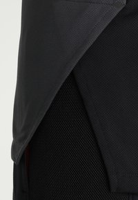 Top sportivo nero con sovrapposizione in rete traspirante e uno strato di base liscio e aderente. Tessuto testurizzato con un taglio elegante e moderno.