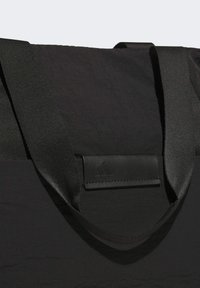 Borsa tote nera con superficie testurizzata, caratterizzata da ampie cinghie in tessuto e un dettaglio in pelle con logo in rilievo. Design elegante e minimalista.