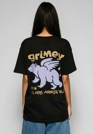 Person mit langen dunklen Haaren trägt ein schwarzes Hemd mit großem, hellviolettem, geflügeltem Bären und beigem Schriftzug "grimey" auf dem Rücken.