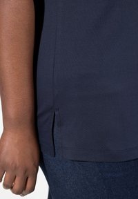 Camiseta azul marino con una abertura lateral, hecha de una tela suave y texturizada. La mano muestra el tono de piel contra la superficie lisa de la camiseta.