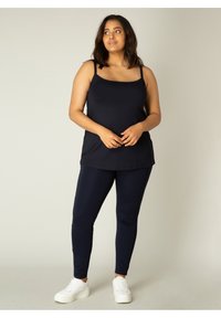 Marineblauw tanktop met dunne bandjes, gecombineerd met marineblauwe leggings. Zachte, rekbare stof met een gladde textuur. Witte sneakers. Eenvoudig, casual ontwerp.