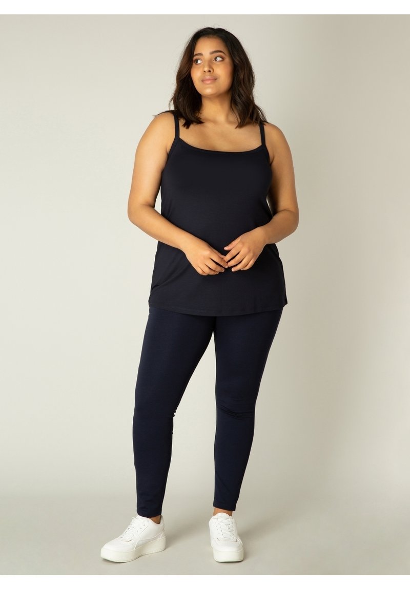 Marineblauw tanktop met dunne bandjes, gecombineerd met marineblauwe leggings. Zachte, rekbare stof met een gladde textuur. Witte sneakers. Eenvoudig, casual ontwerp.