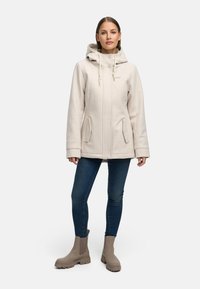 Vaaleanbeige takki hupulla, jossa on kaksi etutaskua ja suora malli. Yhdistetty sinisiin farkkuihin ja taupe-värisiin nilkkasaappaisiin. Sileä pinta.