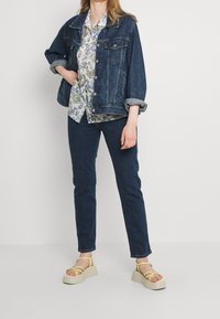 Chaqueta de mezclilla, azul, con mangas enrolladas; camisa de flores en blanco, verde y azul; jeans azul oscuro; sandalias de plataforma crema con tiras amarillas.