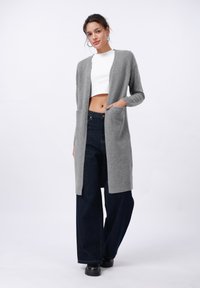 Grijze lange cardigan met open voorkant, twee voorzakken en geribde boorden, gecombineerd met hoge taille donkere denim wijde broek.