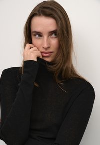 Maglione nero a maniche lunghe con collo alto realizzato in un tessuto morbido con una leggera trasparenza. Presenta maniche aderenti e un colletto alto.