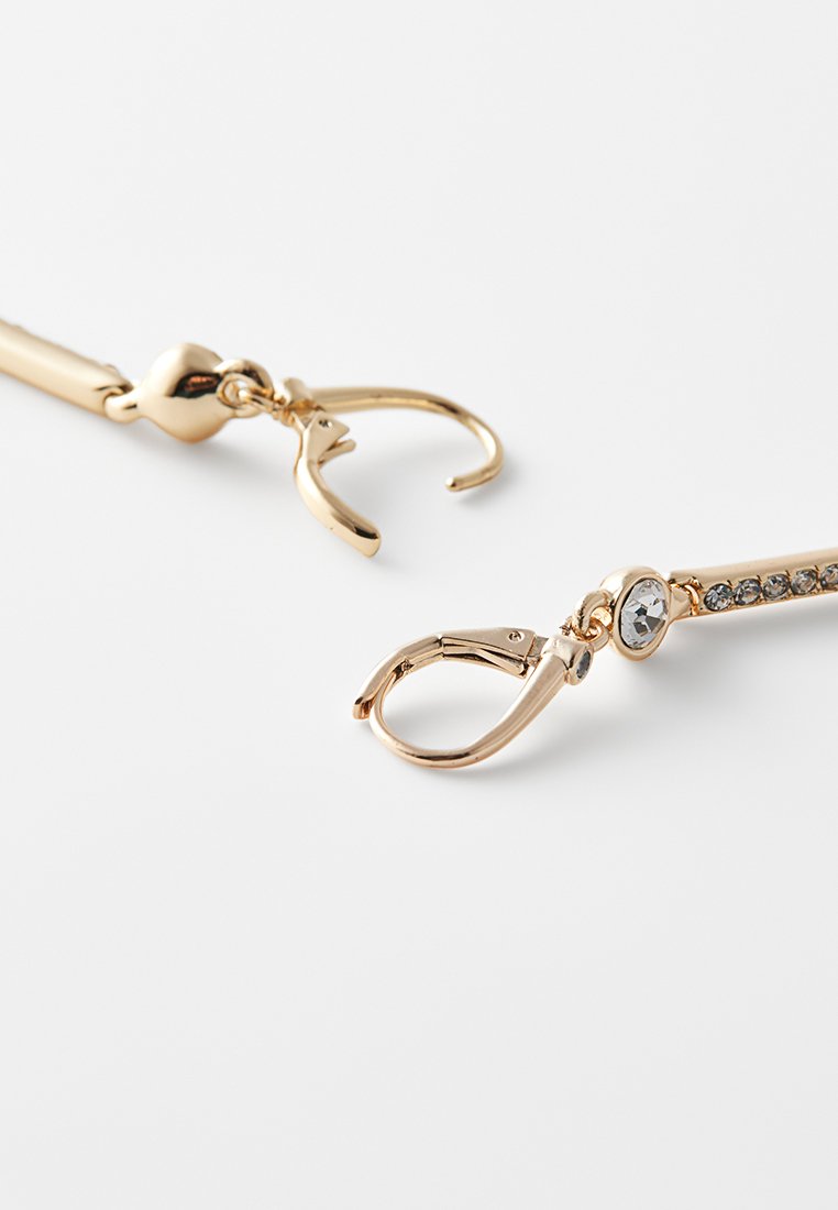 Goldfarbene Ohrringe mit offenen Hakenverschlüssen, einer davon mit einem klaren Edelstein und kleinen eingebetteten Kristallen entlang eines geraden Bar-Designs.