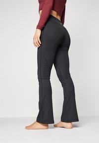 Svarte flagrende leggings laget av elastisk materiale, med en tilpasset midje og sømløst design, vist fra siden med bare føtter.