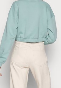 Sudadera corta verde menta con dobladillo acanalado, combinada con pantalones de tiro alto color crema que tienen bolsillos traseros y una tela texturizada.