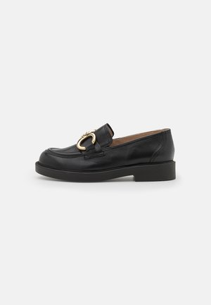 Sorte læder loafers med rund tå, der har et fremtrædende guldhardware-detalje og en lav, sort gummisål.