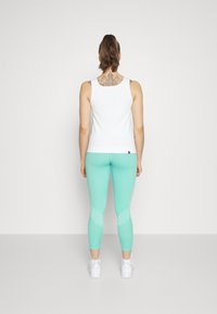 Kobieta z kucykiem, ubrana w białą bezrękawnik, miętowe legginsy, białe trampki i ozdobny tatuaż na górnej części pleców, odwrócona tyłem.