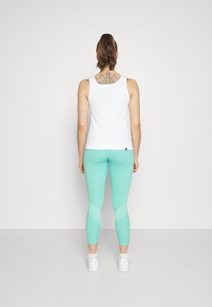 Donna con un ponytail, che indossa una canotta bianca senza maniche, leggings verde menta, scarpe da ginnastica bianche e un tatuaggio ornato sulla parte superiore della schiena, girata di spalle.