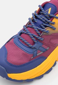 Purple and blue sporty sneaker with yellow accents, textured fabric, padded tongue, and patterned laces. Thick rubber sole for traction.
