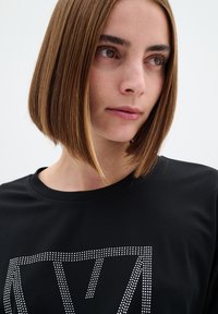 T-shirt noir à manches courtes avec un design géométrique orné de cristaux sur le devant. Tissu doux et col rond.
