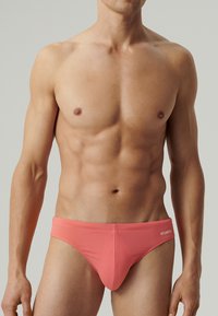 Koralowy bikini w formie fig, wykonany z elastycznego materiału, charakteryzujący się gładką fakturą i markowym akcentem na pasku.