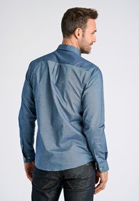 Camisa azul claro abotonada con canesú en un azul más oscuro a contraste, mangas largas y puños ajustables; textura suave y tela de chambray.