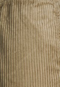 Beige corduroy stof met een verticale ribbelstructuur. Zacht, pluche materiaal met een lichte glans, dat fijne, gelijkmatige ribbels toont.