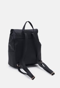 Mochila de poliuretano negra con un diseño estructurado, cierre enrollable, correas ajustables y acentos dorados. Incluye detalle de bolsillo lateral.