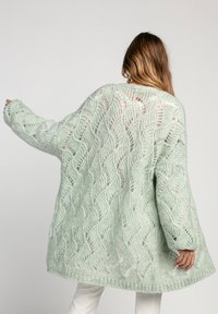 Miętowozielony, dziany, oversize'owy kardigan z falistym wzorem, o luźnym splotcie, szerokich rękawach i zakończeniu opadającym poniżej bioder.