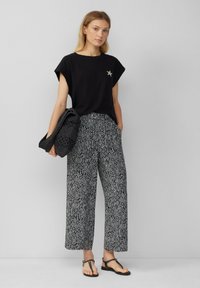 Zwart T-shirt met korte mouwen met een zilveren sterdetail, gecombineerd met wijde gestreepte broek in zwart-wit geometrische ontwerpen.
