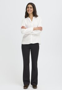 Camicia bianca con colletto, abbinata a pantaloni neri. La camicia ha maniche lunghe e una vestibilità comoda, realizzata in un tessuto leggero.