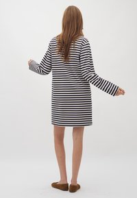 Randig tunika-klänning i marinblått och vitt med långa ärmar. Mjuk tyg, avslappnad passform, sträcker sig ovanför knäna. Bärs med bruna slip-on skor.