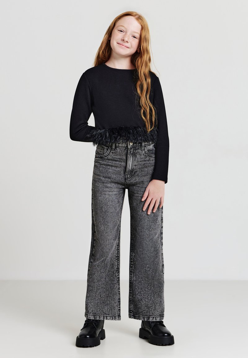 Haut noir à manches longues avec bordure en plumes à la taille, associé à un jean gris taille haute à jambes larges et des bottes noires épaisses.