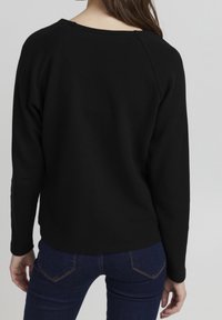 Černý žebrovaný svetr s kulatým výstřihem a raglánovými rukávy. Měkká textura. Spárováno s denimovými džíny s běžnými kapsami.